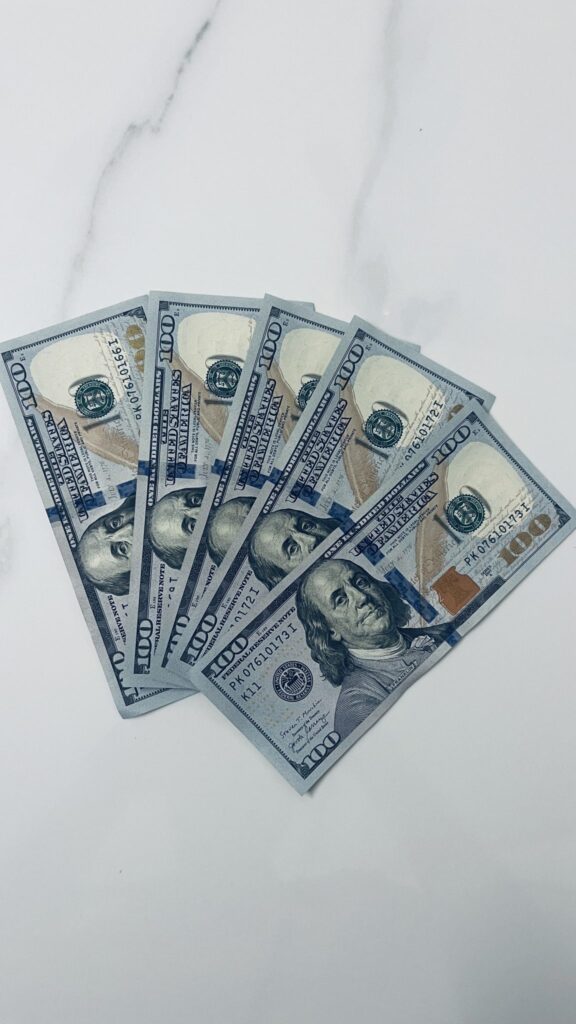 Five one hundred dollar US bills fanned out on a marble background. (Please note rules for using photos of US currency here https://www.bep.gov/currency/currency-image-use)