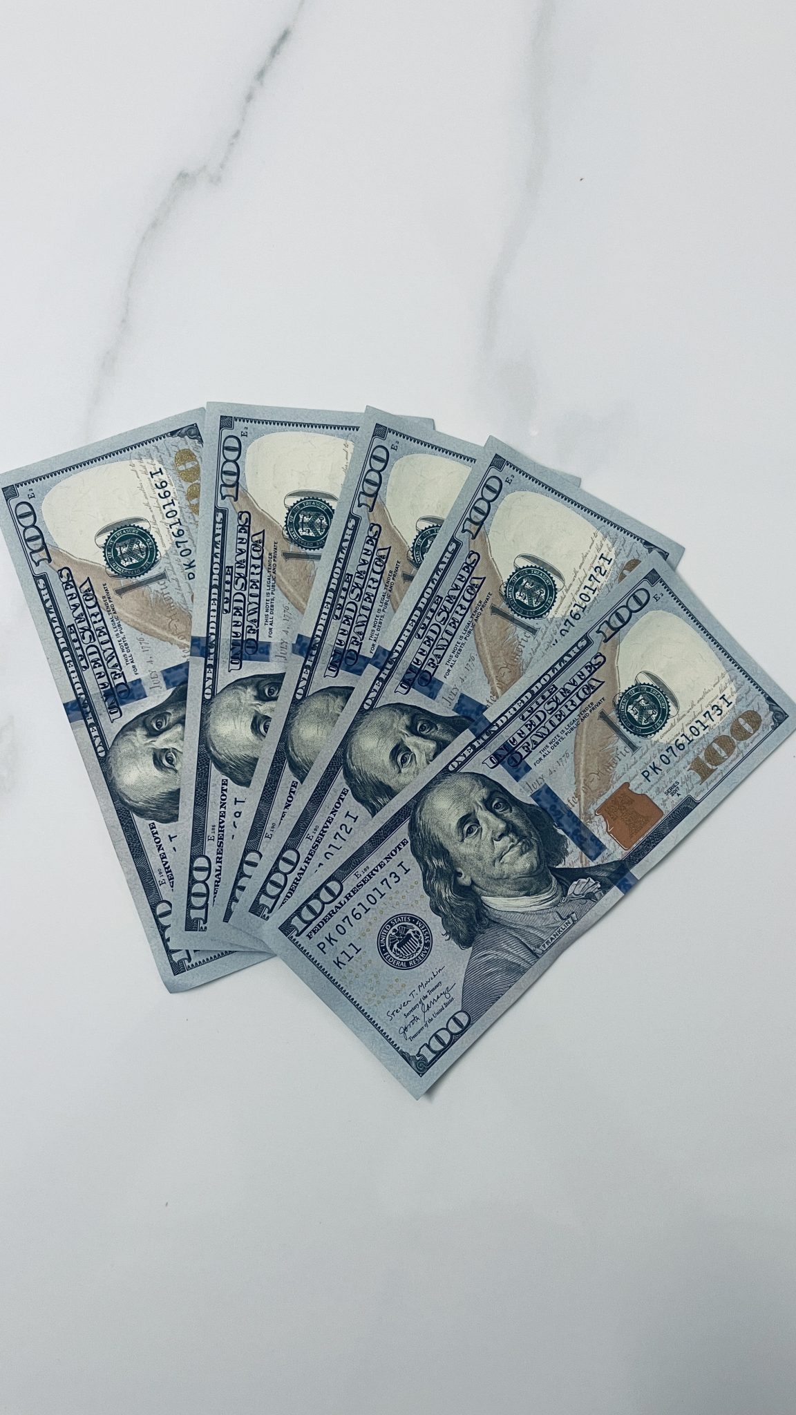 Five one hundred dollar US bills fanned out on a marble background. (Please note rules for using photos of US currency here https://www.bep.gov/currency/currency-image-use)