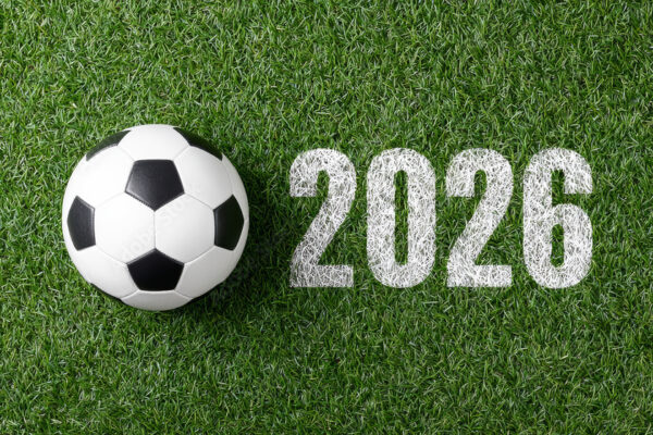 Classic soccer ball lying on the green grass of a playing field with the number 2026 painted on the ground