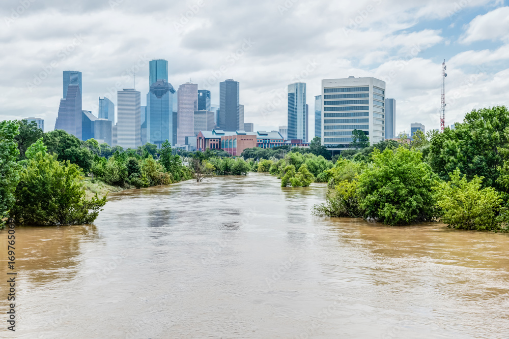 High and fast water rising in Bayou River with downtown Houston in background under cloud blue sky. Heavy rains from Harvey Tropical Hurricane storm caused many flooded areas in greater Houston area.
